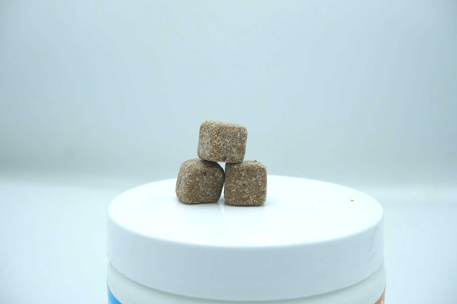 Close up of two PawSafe honey chicken flavor probiotic soft chews on a kitchen surface